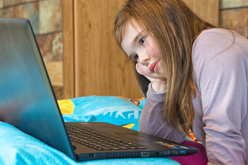 little girl looks intently into the laptop on the bed in the bedroom

