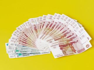 Cash in banknotes spread out like a fan. Yellow background.