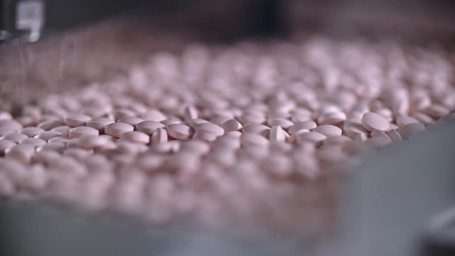 Drugs factory, close up slow motion footage of many tablets and pills. Pink tablets on a conveyor line with the top view. Pharmaceutical industry concept.