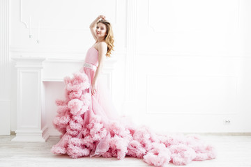 Gorgeous woman portrait in a long pale pink ruffled dress train in a white classic style room....