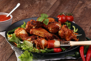 barbecue chicken wings close up on wooden tray with red spice sauce and salad