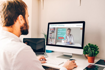 Young man in front of computer with healthcare videoblog on the screen.