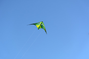 triangular yellow with green kite floating in the blue sky
