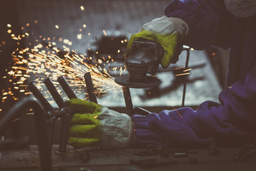 Close-up of a worker in a small manufacture, grinding a piece of welded tube-pipe.