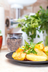 Delicious baked fried potatoes with parsley in black plate on table in the kitchen. Shallow depth of field. Coloring and processing photo.