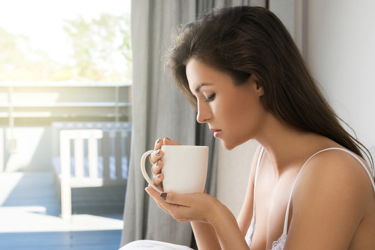 Beautiful woman drinking coffee or tea in bedroom