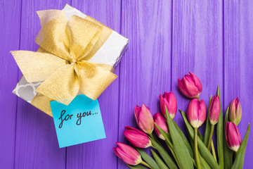 Purple tulip bouquet, blank greeting card for you and gift boxes. Top view over purple wooden table