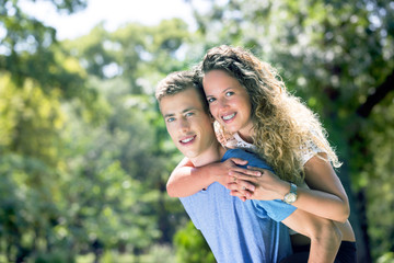 young couple having piggyback in a park in summer