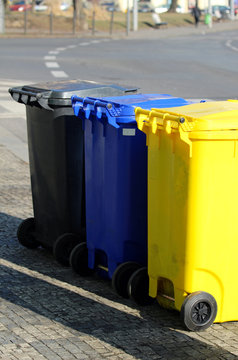 three different multicolored dustbins on the street