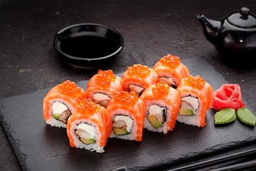 Japanese cuisine. Salmon sushi roll on a stone plate over concrete background.