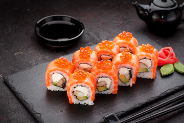 Japanese cuisine. Salmon sushi roll on a stone plate over concrete background.