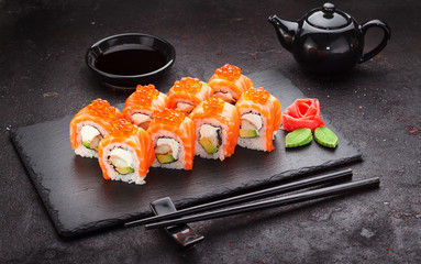 Japanese cuisine. Salmon sushi roll on a stone plate over concrete background.
