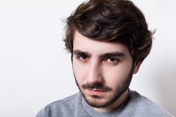 Fototapeta premium Headshot of handsome hipster with black beard and stylish hair looking at camera with serious face expression, squinting his eyes. Portrait of masculinity. People and emotions.