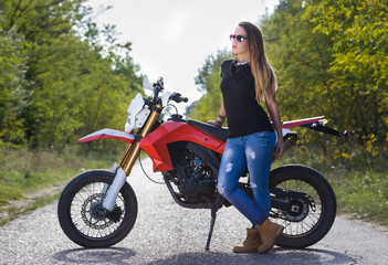 Naklejka na ściany i meble young long hair brunette woman posing with motorbike in the middle of the road in a forest