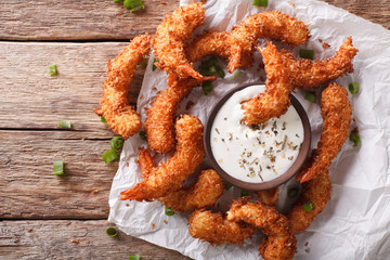 Delicious fried shrimp in coconut chips close-up and sauce on the table. Horizontal top view