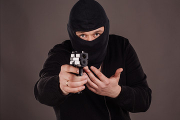 Burglar or robber aiming with pistol. man in black mask