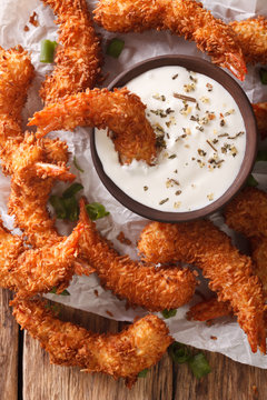 fried coconut shrimp close-up and a cream sauce on the parchment on the table. vertical top view