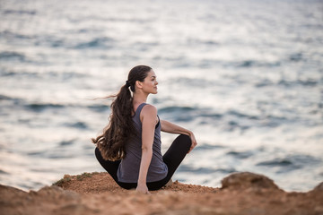 Fototapeta na wymiar Yogi girl does twisting on a cliff by the sea