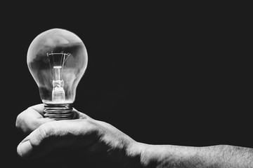 Black and white photo. Hand holding light bulb on black background.