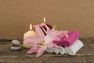 aBeautiful composition with two candles, stack of spa stones, pink lily and towels on wooden background, spa treatment conceptpink lily and towels on wooden background