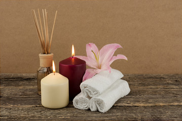Beautiful composition with burning candles, pink lily and spa towels on wooden background, wellness and spa concept