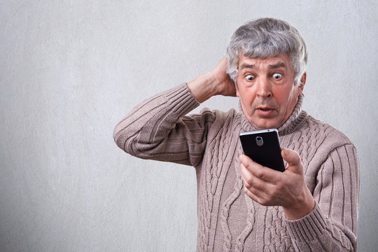 Portrait of surprised senior man looking with wide open eyes into his smartphone being shocked by what he sees on his cell phone. Human face expressions. Surprise, astonishment, wonder