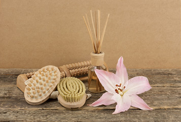 Beautiful composition with aromatic oil, pink lily and massage brushes on wooden background, weight loss and body care concept