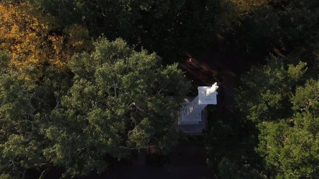 Aerial Shot Descending Between the Trees Focused on an Alabaster Statue in a Tow