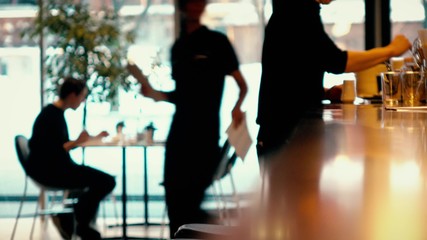 Defocused visitor using his smartphone and waiters at work in a modern cafe