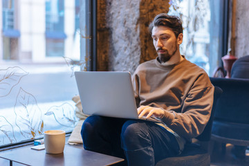 Young freelance designer working on new project with notebook computer while sitting at cozy cafe, Portrait of young businessman working on modern laptop in modern cafe during online meeting