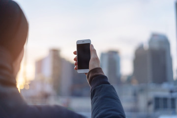 Man holding modern smart phone with big city on the background, Man taking pictures the City on sunset on his phone, blurred background, shallow DOF