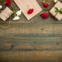 Frame with red roses, gift box, craft paper and twine on wood background. Flat lay, top view. Floral background, workspace