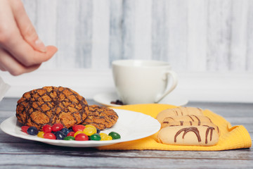 oatmeal cookies and multi-colored sweets in a plate, mug in the background