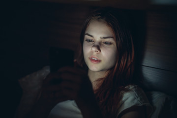 woman lies in bed and looks into phone