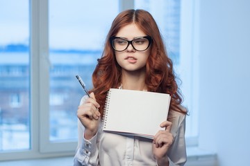 red-haired woman bites her lip and holds a notebook and a pen in her hand