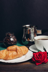 Croissant in a plate, a flower and a mug with a drink