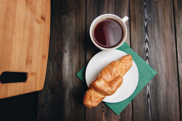 cup with a drink and a croissant in a plate, top view