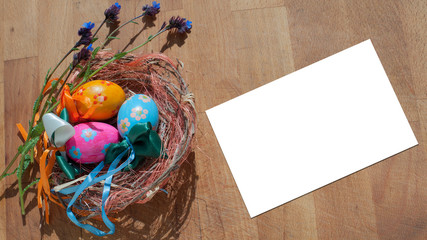 Le uova pasquali dipinti a mano nel nido di paglia e cartolina bianca sul tavolo di legno