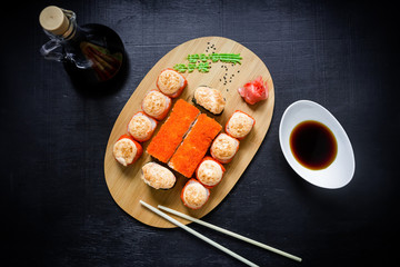Top view. Flat lay. Japanese food, catering, roll plate or platter set. Sushi roll with chopsticks, ginger, soy sauce, wasabi at dark background.