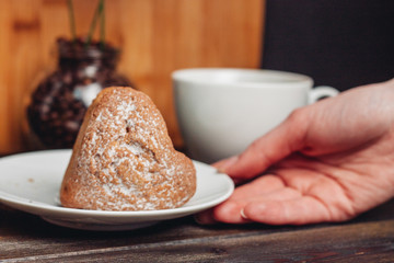 cupcake sprinkled with powdered sugar, a female hand and a cup in the background