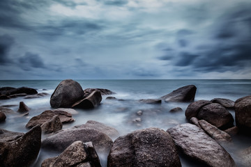 Dark rocks in a blue ocean under cloudy sky in a bad weather., Long exposure photography. - Powered by Adobe