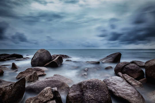 Dark rocks in a blue ocean under cloudy sky in a bad weather., Long exposure photography.