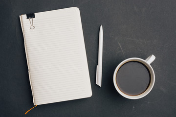 a notebook with a clip, a white pen and a cup with a drink