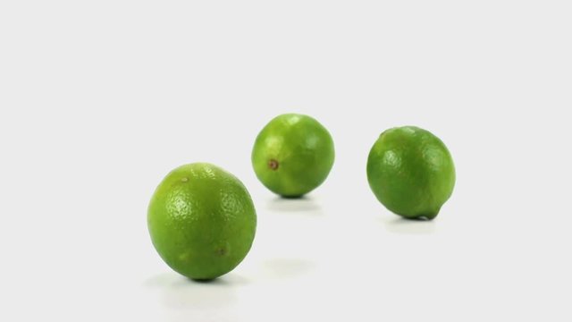 Three limes tumble and fall in slow motion onto a white cyc
