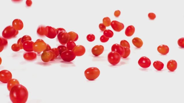 Cherry tomatoes tumble and fall in slow motion onto a white cyc