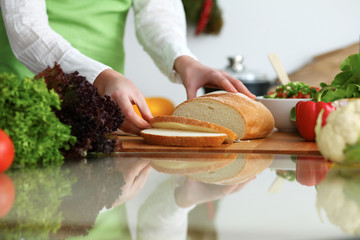 Closeup of human hands slicing bread in kitchen on the glassr table with reflection. Healthy meal and vegetarian concept