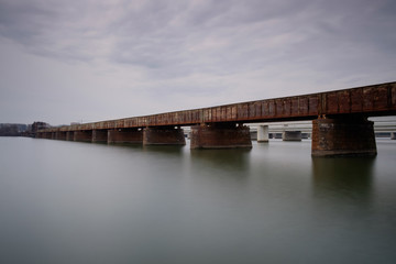 Rusty train bridge over water on a cloudy day
