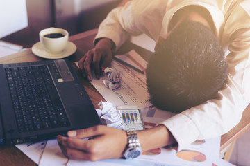Exhausted and tired businessman sleeping in a cafe with laptop and coffee cup on the table.