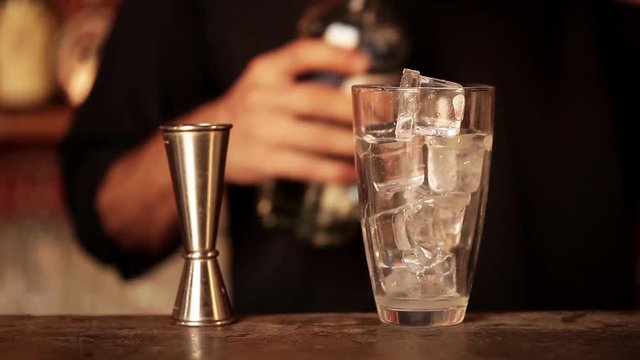 Bartender pouring double shot of vodka over ice in cocktail shaker