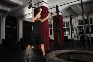 Fototapeta premium Fitness Man Hitting A Tractor Tire With Hammer